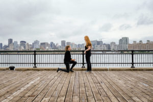 Woman proposing to her girlfriend on a boardwalk with the Montreal skyline behind them